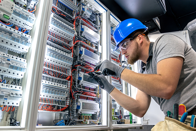 Male electrician in uniform working in a switchboard. Electricity.